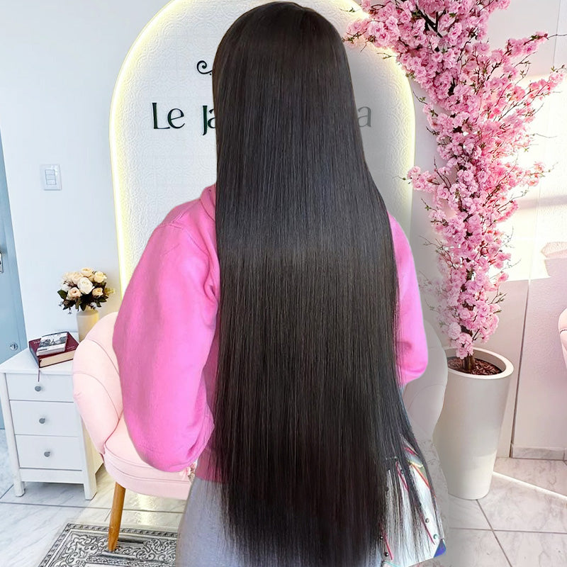 Person with long straight hair wig in a salon setting with pink flowers and a mirror.
