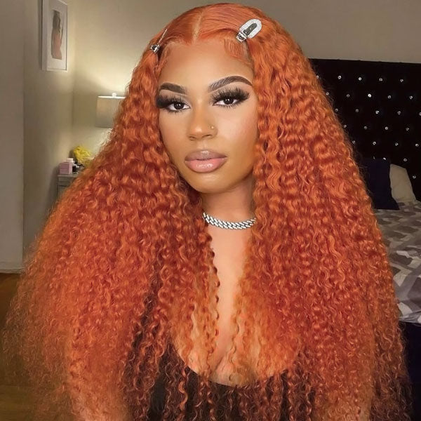 Woman wearing a thick curly ginger orange lace front wig with middle part and hair clips. The wig is a 100% human hair pre-bleached wig from Ishow Beauty, shown in a bedroom setting.