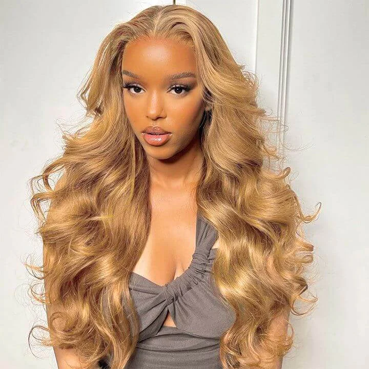 Light #27 honey blonde human hair wig with body wave texture showcased on a woman with hoop earrings and wearing a mustard yellow top.