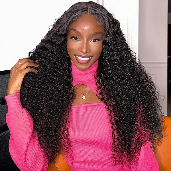 Woman with long kinky curly hair wearing a black top, showcasing Ishow Kinky Curly Ready To Wear Wig with 13x6 HD Lace Frontal, styled in a middle part, posing indoors with floral wall decor.